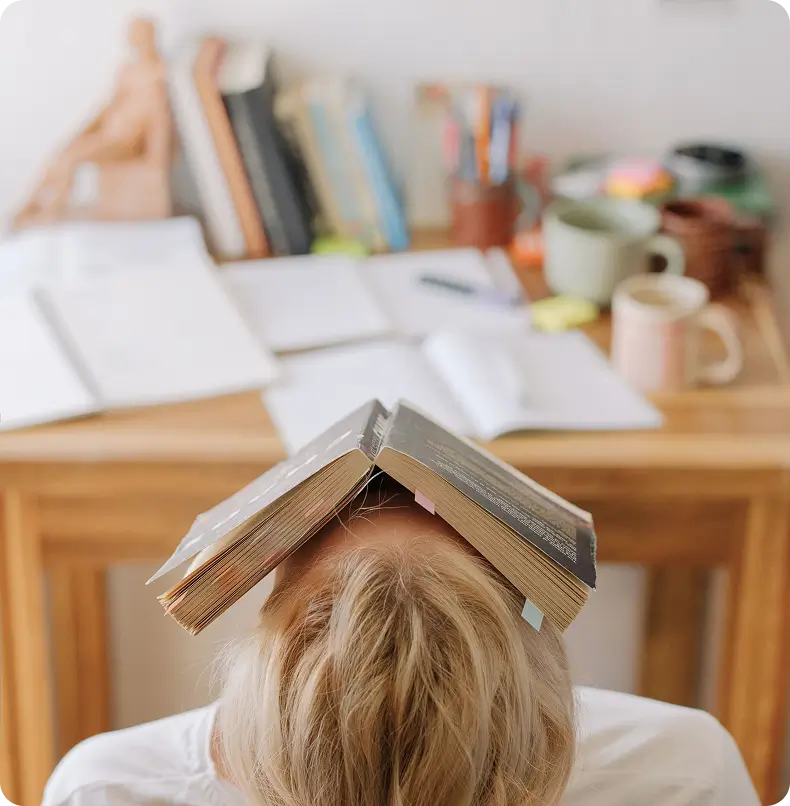 Writer frustrated with a book laying across her face, stuck on her novel
